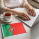 Trabalho em Portugal - Mesa de trabalho com uma xícara da de chá, uma bandeira e um notebook sobre a mesa