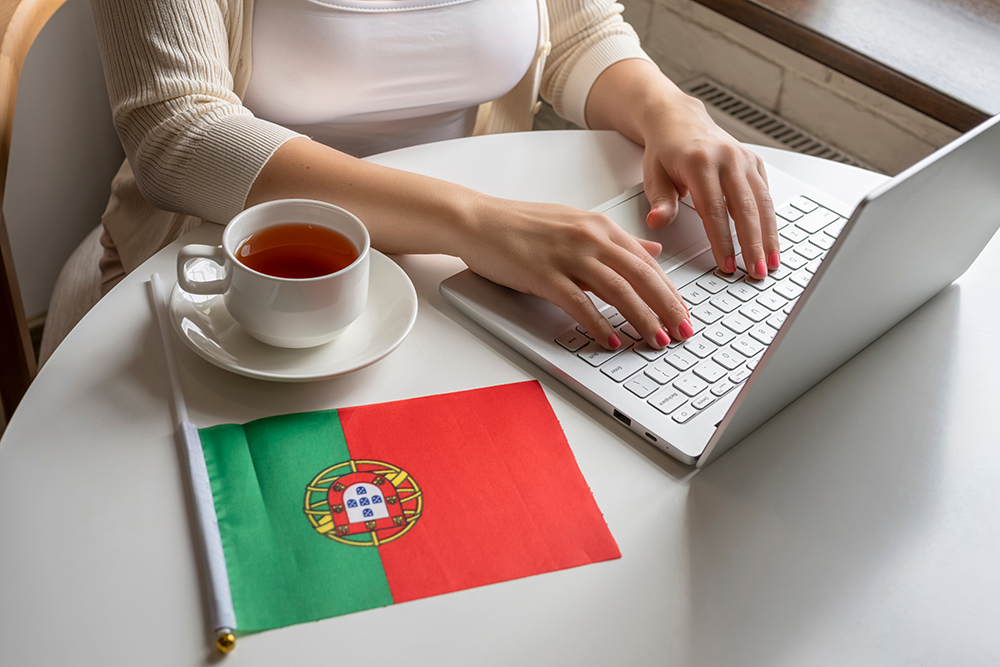 Trabalho em Portugal - Mesa de trabalho com uma xícara da de chá, uma bandeira e um notebook sobre a mesa