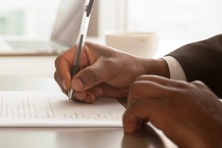 Empresário africano sentado na mesa detém papel de contrato de assinatura de caneta