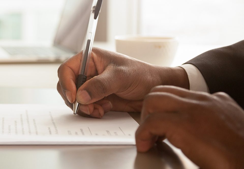 Empresário africano sentado na mesa detém papel de contrato de assinatura de caneta
