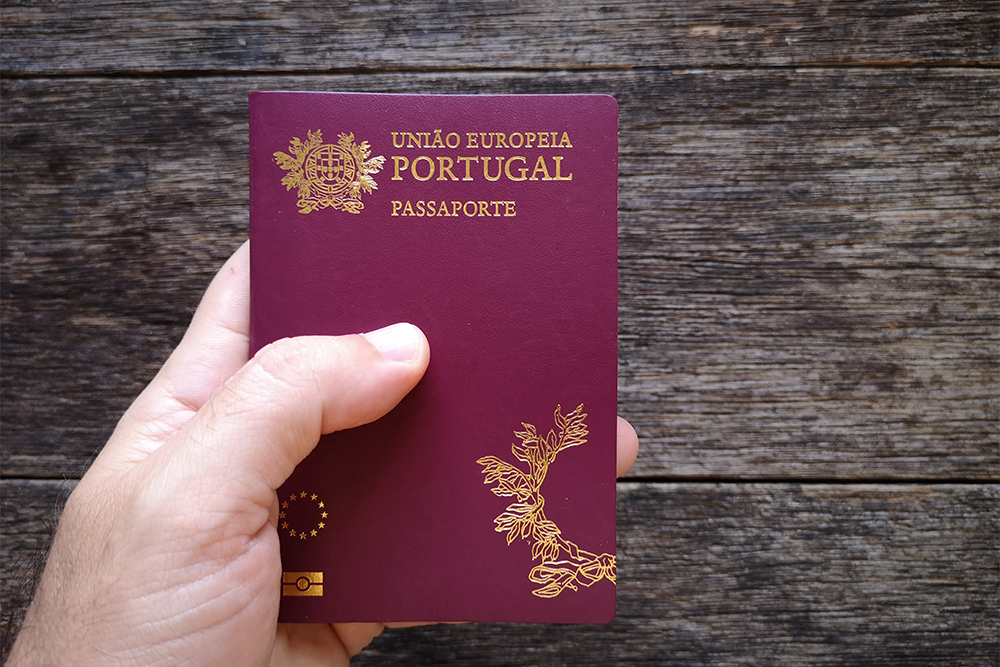 Mão segurando o passaporte português com fundo de madeira